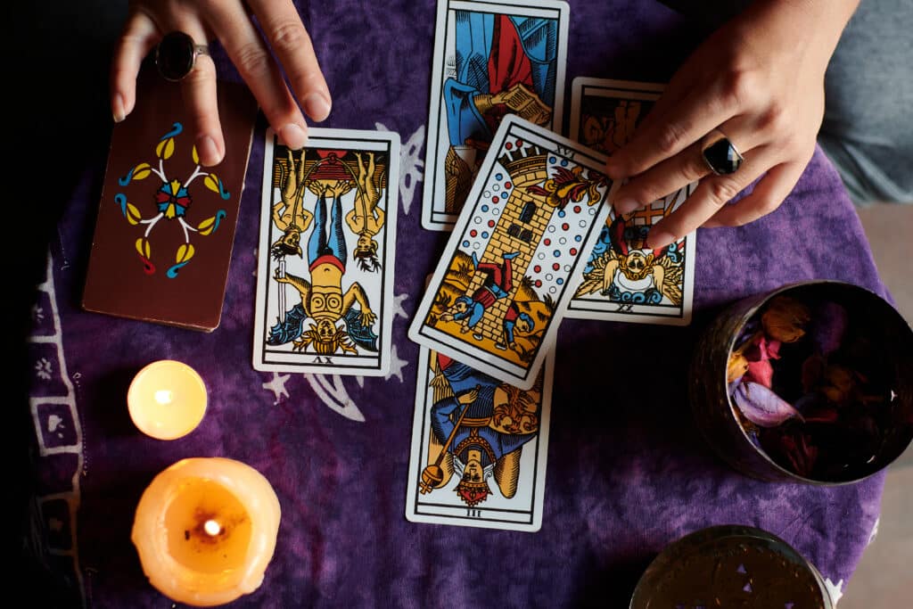 Close-up of a fortune teller reading tarot cards on a table with purple tablecloth มูเตลูจนเกินเหตุ